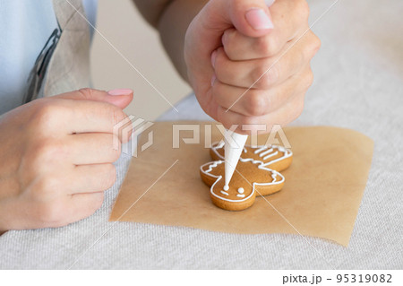 Women's hands decorate sugar icing homemade traditional New Year's cookies snowflake gingerbread man Women's hands decorate sugar icing homemade traditional New Year's cookies snowflake gingerbread man 95319082