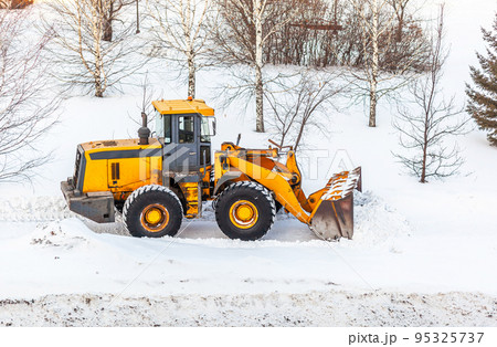 Snow clearing. Tractor clears the way after heavy snowfall. A large orange tractor removes snow from the road and clears the sidewalk. Cleaning roads in the city from snow in winter. Snow clearing. Tractor clears the way after heavy snowfall. A large orange tractor removes snow from the road and clears the sidewalk. Cleaning roads in the city from snow in winter. 95325737