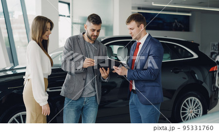 Handsome young guy is signing sale and purchase agreement in car dealership 95331760
