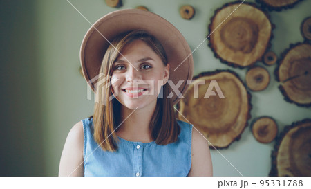 Close-up portrait of attractive young woman with blond hair wearing trendy hat and denim top looking at camera and smiling. Modern people and positive emotions concept. 95331788