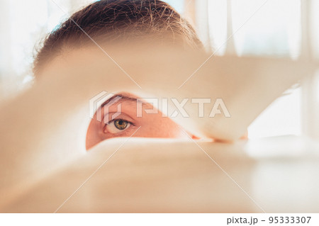 A person looks with one eye through a rolled-up sheet of a book. Concept of education and new knowledge A person looks with one eye through a rolled-up sheet of a book. Concept of education and new knowledge 95333307