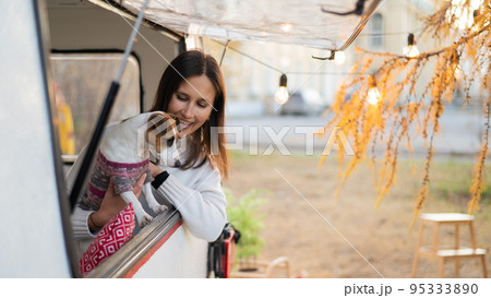 Caucasian woman looks out of the window of the van while hugging her dog Jack Russell Terrier. Travel in a camper in autumn. 95333890