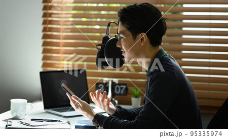 Side view of young asian man recording conversation for her channel to recording podcast in small home studio Side view of young asian man recording conversation for her channel to recording podcast in small home studio 95335974