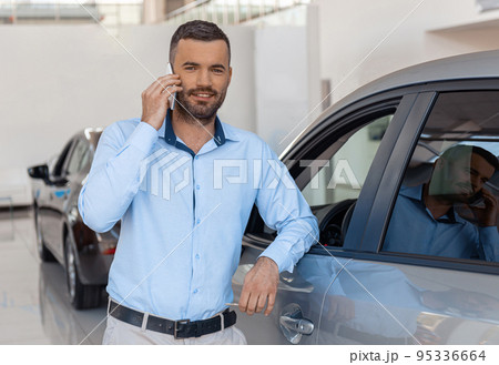 Young male consultant standing in auto show office and talking phone. Blurred background Young male consultant standing in auto show office and talking phone. Blurred background 95336664