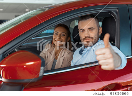 Happy young couple chooses and buying a new car for the family in the dealership Happy young couple chooses and buying a new car for the family in the dealership 95336666