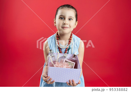 little black-haired fashionista holds a bag of cosmetics in her hands. funny photo shoot of a girl in the studio on a red background 95338882