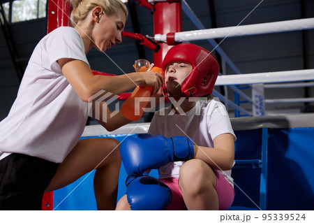 Coach assist to little athlete. Beginner boxer in sport uniform drinking water after workout at sports gym. Concept of sport, studying, achievements, healthy lifestyle. Coach assist to little athlete. Beginner boxer in sport uniform drinking water after workout at sports gym. Concept of sport, studying, achievements, healthy lifestyle. 95339524