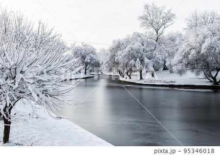 winter park, trees and a bench covered with snow, the river partly covered with ice 95346018