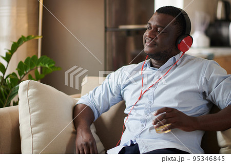 Portrait of happy man drinking glass of whiskey and listening to music in headphones Portrait of happy man drinking glass of whiskey and listening to music in headphones 95346845