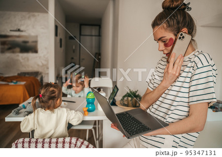Busy remote worker and her children in the kitchen 95347131
