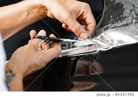 Car wrapping specialist wraps a car with adhesive film in car detailing service Car wrapping specialist wraps a car with adhesive film in car detailing service 95347202