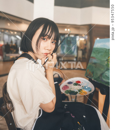 Portrait of happy young adult asian woman painting brush on canvas at workshop art lesson class. 95347550