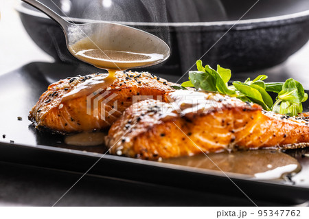 The spoon finishes the portion by pouring a demiglas sauce over the salmon fillets. 95347762