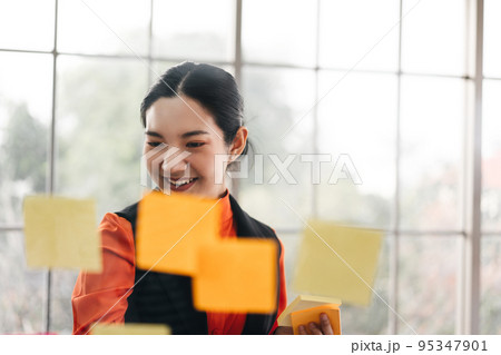 Business asian woman use post it stick on glass board with window light. 95347901