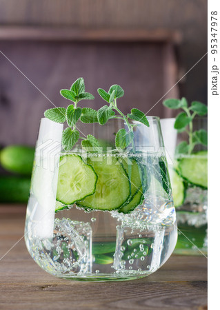 Detox drink. Water with pieces of cucumber, ice and mint leaves in a transparent glass on a wooden table 95347978