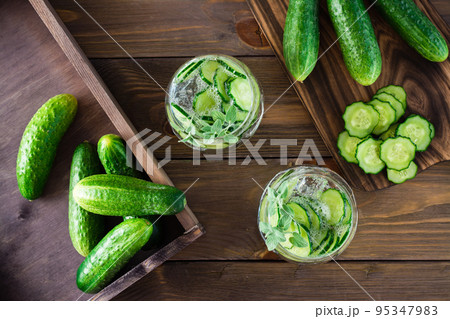 Detox drink. Water with pieces of cucumber, ice and mint leaves in transparent glasses on a wooden table. Top view 95347983