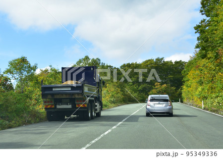 急勾配の坂道を登るダンプを追い抜く乗用車 95349336