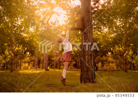 little cute girl with pigtails is trying to reach the birdhouse among the autumn foliage 95349553