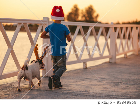 Holidays at beach concept with child and dog wearing Christmas and New Year costumes at seafront Holidays at beach concept with child and dog wearing Christmas and New Year costumes at seafront 95349859