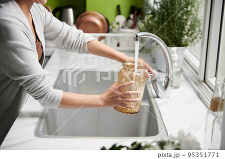 Cropped image of woman filling vase with tap water 95351771