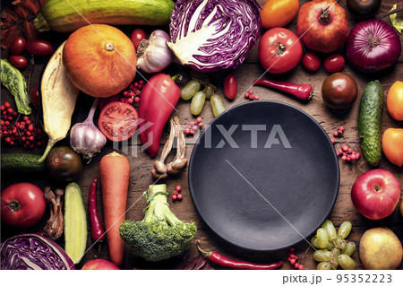 A rich table with an assortment of fruits and vegetables of fresh harvest. an empty black plate on a flat lay wooden table 95352223