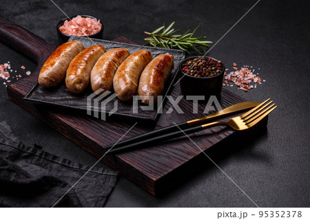 Tasty grilled sausages with spices and herbs on a black slate plate 95352378