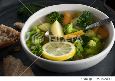 Vegetarian vegetable soup with carrots, broccoli and parsley in a light bowl on a metal tray on a wooden table 95352841
