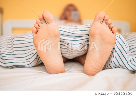 Woman feet on the bed under white blanket. Sleeping and relax concept. Vacation and Holiday theme Woman feet on the bed under white blanket. Sleeping and relax concept. Vacation and Holiday theme 95355256