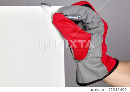 A hand in a red protective glove inserts a confirmation into a hole in a furniture shield. Assembly and repair of furniture 95355406