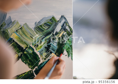 Young woman artist paints with a spatula on the canvas 95356156