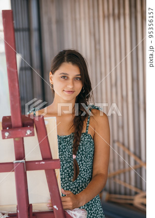 Young beautiful artist stands near an easel with a canvas 95356157