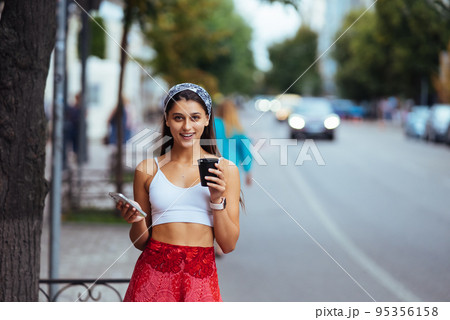 Woman in the street drinking morning coffee and use smartphone. 95356158