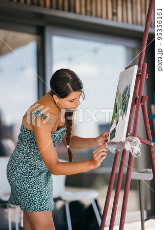 Young woman artist paints with a spatula on the canvas 95356161