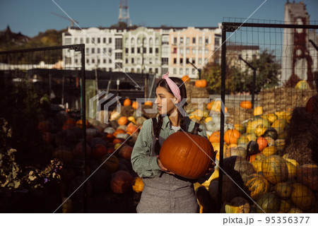 Happy farmer woman in a denim jumpsuit holds ripe pumpkin 95356377