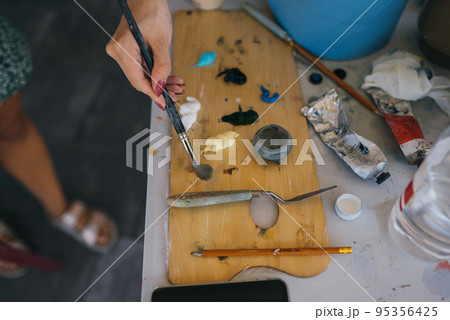 Artist mixes paints with a brush on a palette Artist mixes paints with a brush on a palette 95356425