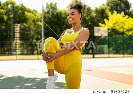 Sporty black woman in yellow sportswear stretching leg 95357128