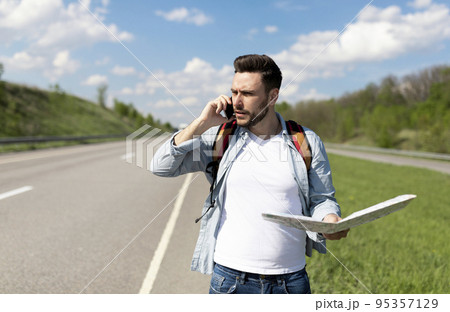 Handsome young man standing on road with map, feeling lost, calling on smartphone, checking travel options, empty space 95357129
