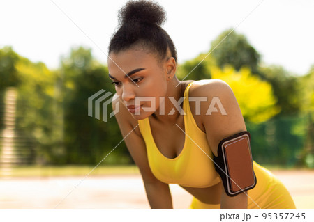 Sporty black woman in yellow sportswear resting breathing after run 95357245