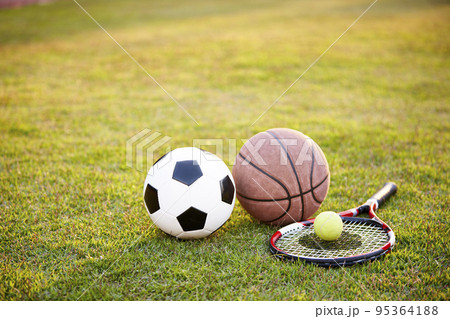 football soccer ball basketball tennis ball and racket laid on grass at sunset 95364188
