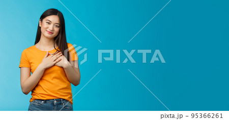 Tender lovely friendly-looking asian girl with dark short haircut touch chest press palms heart, look with admiration and tenderness, smiling joyfully, contemplate heartwarming scene, blue background 95366261