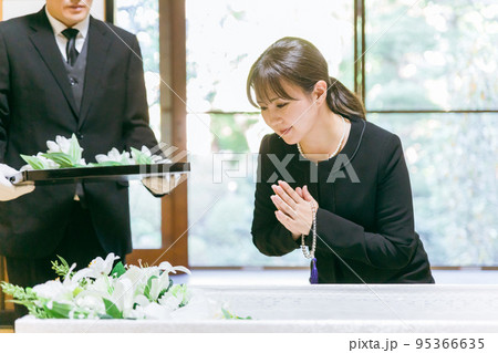 お葬式の納棺で花入れの儀をする日本人女性（笑顔・合掌） 95366635