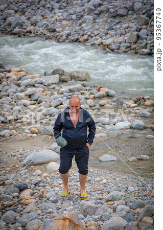 A man stands by a mountain river and holds a stone in his hands. 95367749