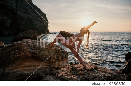 Young woman with black hair, fitness instructor in pink leggings and tops doing stretching and pilates on volcanic rocks near the sea on sunset. Female fitness yoga routine concept. Healthy lifestyle. Young woman with black hair, fitness instructor in pink leggings and tops doing stretching and pilates on volcanic rocks near the sea on sunset. Female fitness yoga routine concept. Healthy lifestyle. 95368504