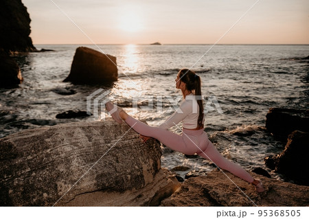 Young woman with black hair, fitness instructor in pink leggings and tops doing stretching and pilates on volcanic rocks near the sea on sunset. Female fitness yoga routine concept. Healthy lifestyle. 95368505
