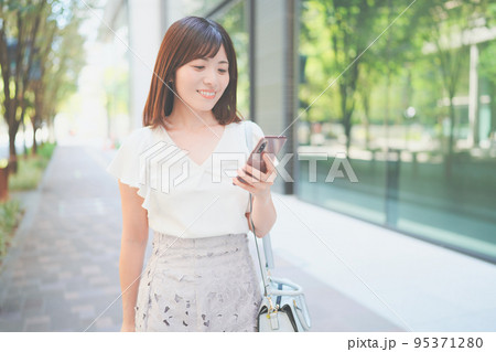 オフィス街でスマートフォンを持って歩くキャリアウーマン 95371280