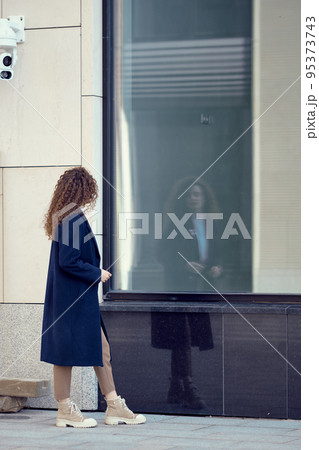 Woman walks along the sidewalk and looks at her reflection in the windows 95373743
