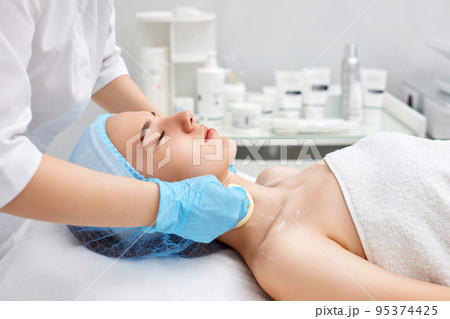 beautician cleanses skin of beautiful woman with a sponge. beautician cleanses skin of beautiful woman with a sponge. 95374425