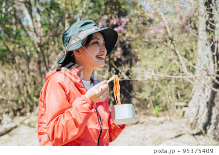 登山でメスティンを使った料理を食べる女性 95375409
