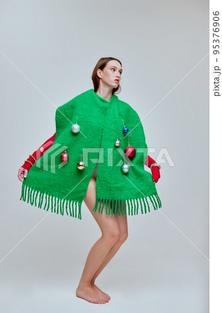 Portrait of young beautiful girl wearing big green scarf with decorations isolated over grey background. Christmas style 95376906
