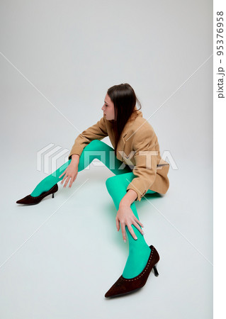 Portrait of young girl posing in green tights, oversized jacket and heels isolated over grey studio background. Stylish look. Portrait of young girl posing in green tights, oversized jacket and heels isolated over grey studio background. Stylish look. 95376958